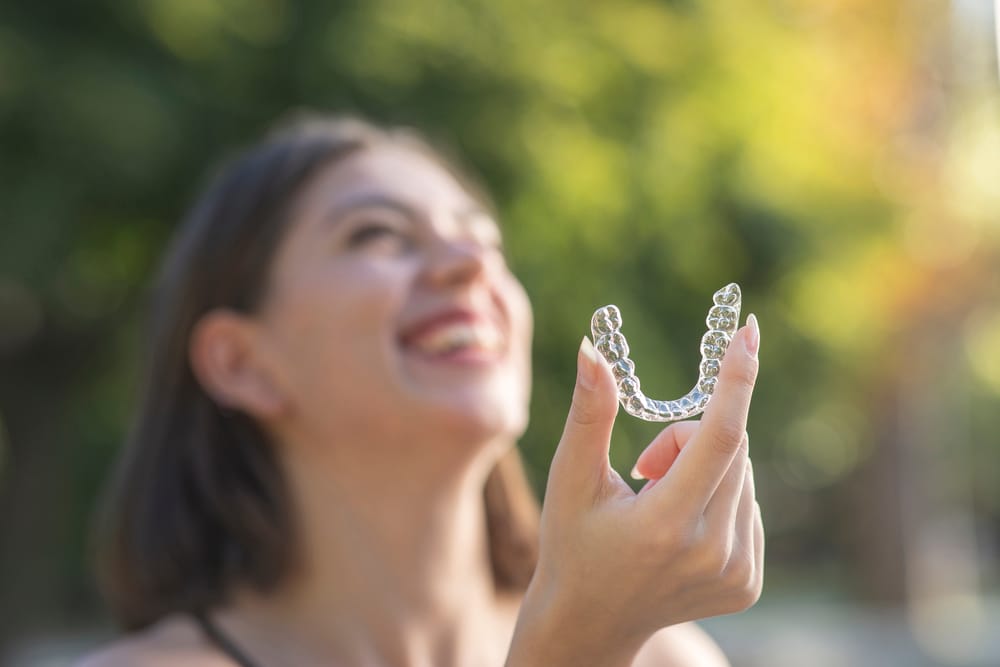 Woman holding clear aligners outdoors while smiling, showcasing discreet orthodontic treatment results in San Diego – Clear Aligners San Diego