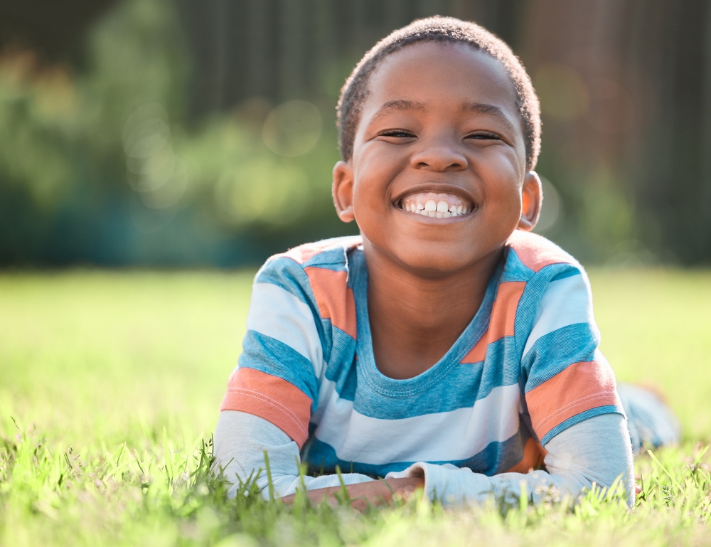Happy child lying on grass and smiling widely, showing bright, healthy teeth and reflecting positive pediatric dental care - Pediatric Dentistry San Diego