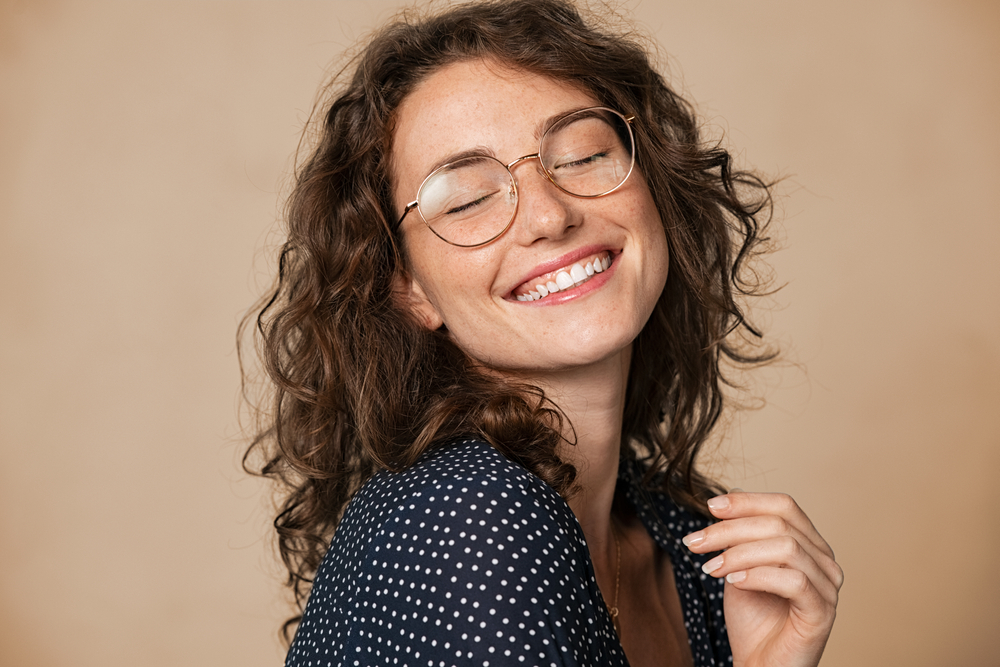 Smiling woman with curly hair and glasses showing bright, even teeth, representing confidence and natural-looking dental bridge results - Dental Bridges San Diego