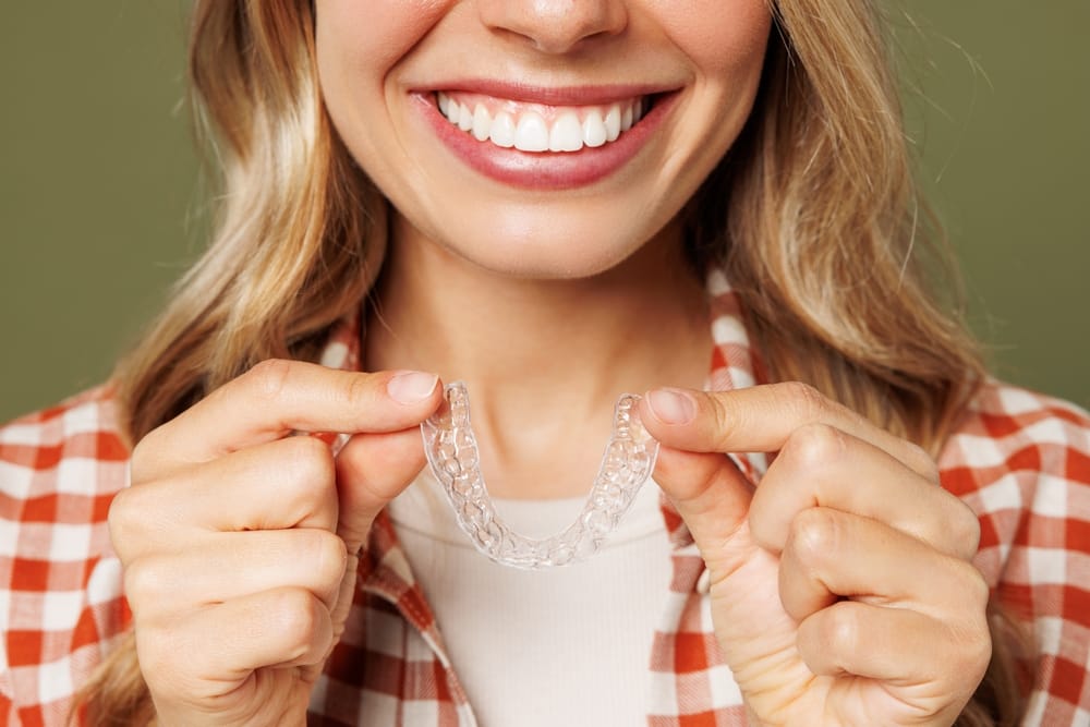 Woman holding clear aligner trays and smiling to show invisible orthodontic treatment results in San Diego – Clear Aligners San Diego