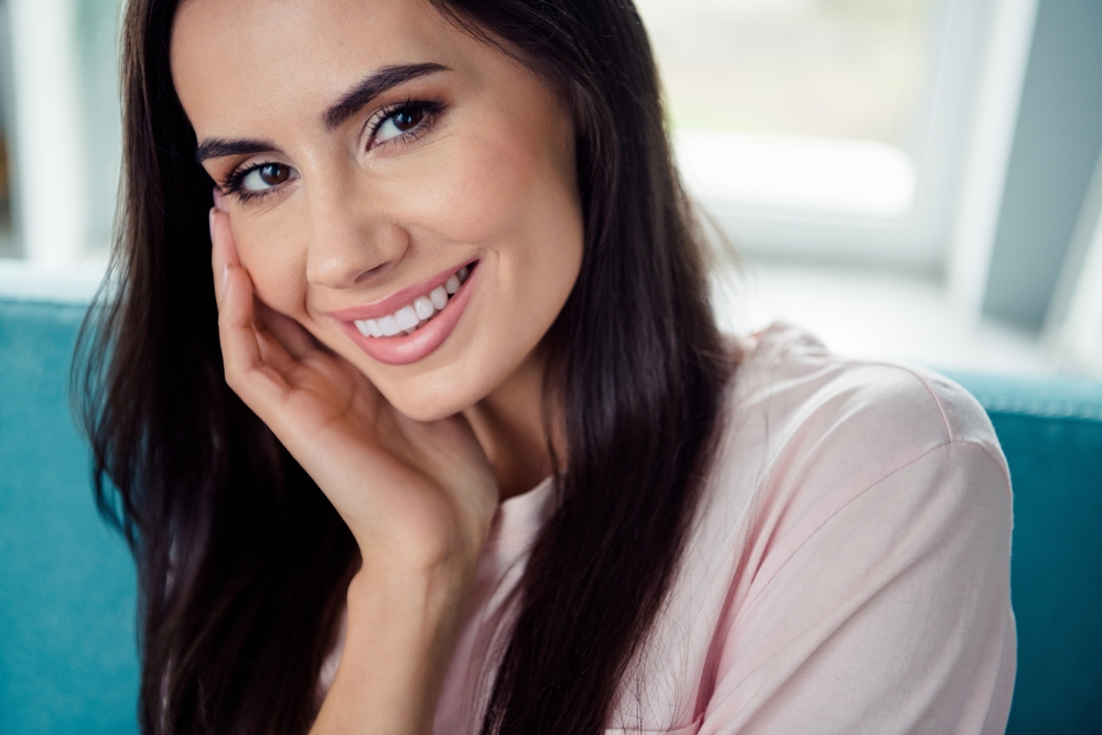Portrait of a smiling woman with straight, white teeth resting her face on her hand, highlighting natural-looking dental bridge results - Dental Bridges San Diego
