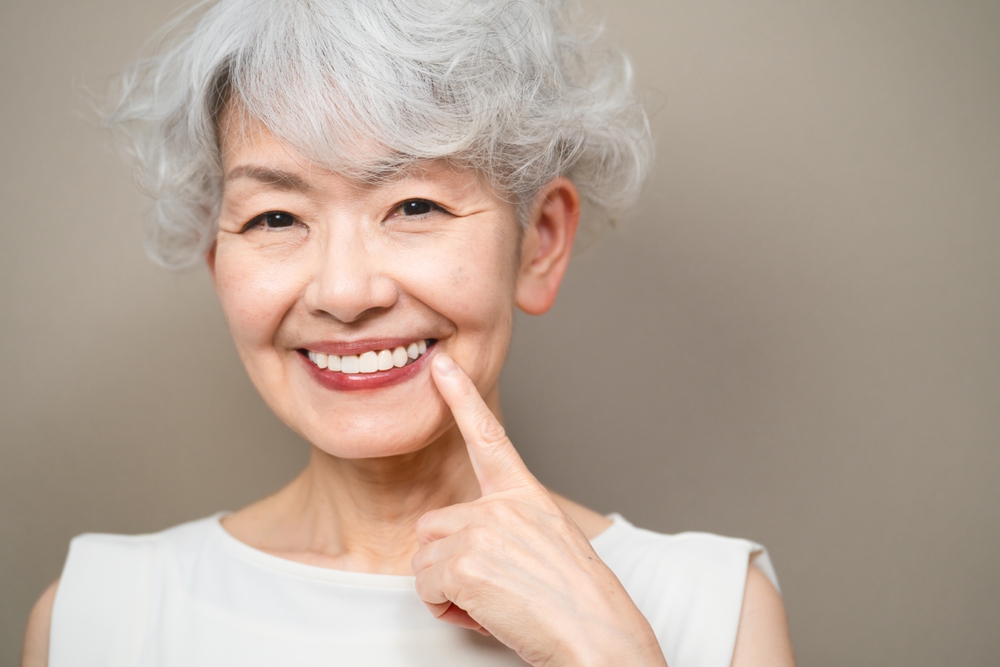 Older woman pointing at her healthy, restored teeth after dental crowns treatment in San Diego – Dental Crowns San Diego 