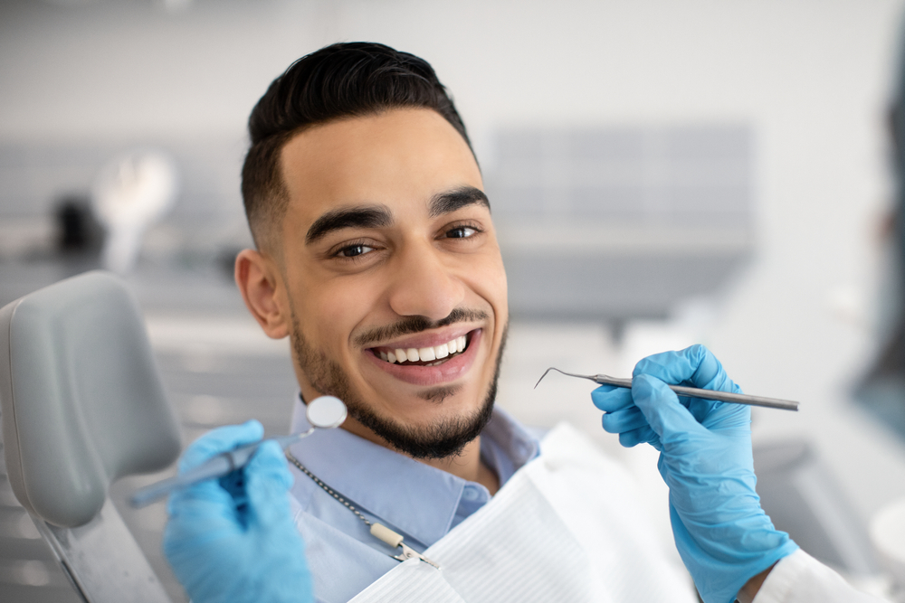 Smiling male patient in dental chair with dentist holding tools, showcasing successful and natural-looking dental implant results - Dental Implants San Diego