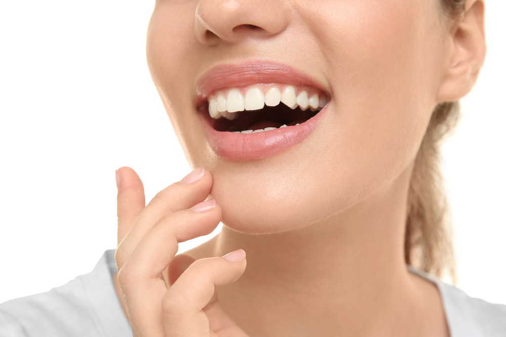 Close-up of a woman smiling with healthy, white teeth and hand near chin, showcasing natural-looking dental restoration results - Dental Crowns San Diego