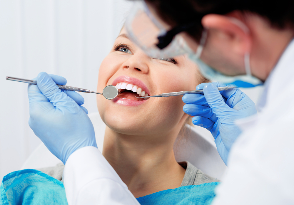 Dentist performing a dental examination with mirror and tools while patient smiles comfortably, representing safe and effective root canal treatment - Root Canal San Diego